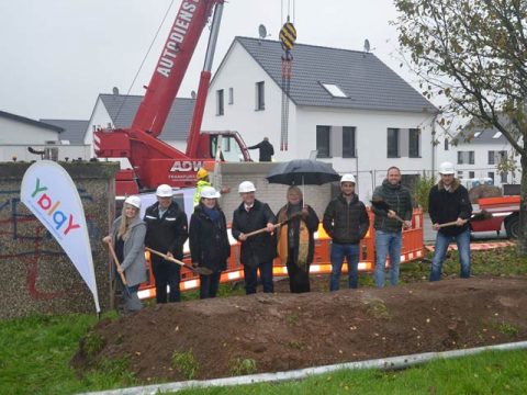 Gruppe Personen stehen in einer Reihe mit Spaten und Bauhelmen in Baugrube für Glasfaseraubau Limeshain