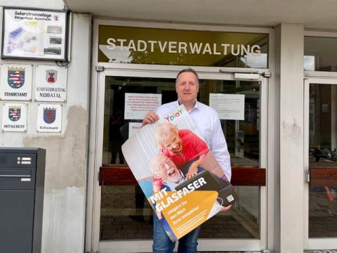 Michael Hahn, Bürgermeister von Niddatal steht vor Stadtverwaltung und hält Werbeplakat der Yplay