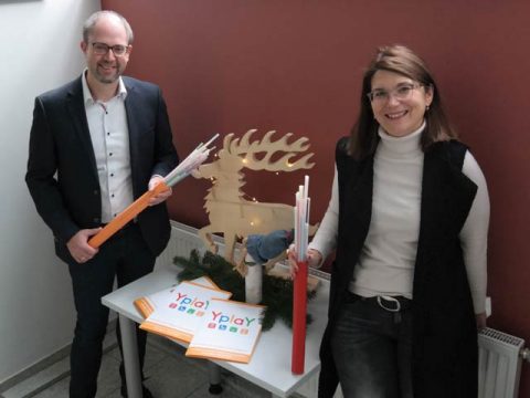 Peer Kohlstetter und Cecilia Reichert-Dietzel stehen an Tisch mit Weihnachtsdeko und Yplay-Werbung und halten Glasfaser-Leerrohre, Glasfaserausbau Ranstadt