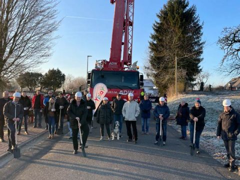 Gruppe Personen mit Bauhelmen stehen vor großem Kran, Glasfaserausbau Ronneburg