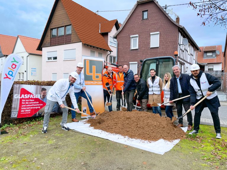 Gruppe von Personen stehen an einer Straße vor einem Sandhaufen mit Bauhelmen und Spaten neben Fahne der Firma Yplay zum Spatentisch in Altenstadt Höchst