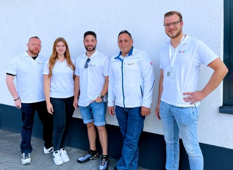 Gruppe von 5 Personen mit weißen T-Shirts und Jacken mit Yplay-Logo vor weißer Wand
