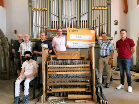 Gruppe Personen steht vor einer Kirchenorgel, 2 davon halten Spendenquittung von der Firma Yplay für die Renovierung der Ratzmannorgel in Bad Soden-Salmünster