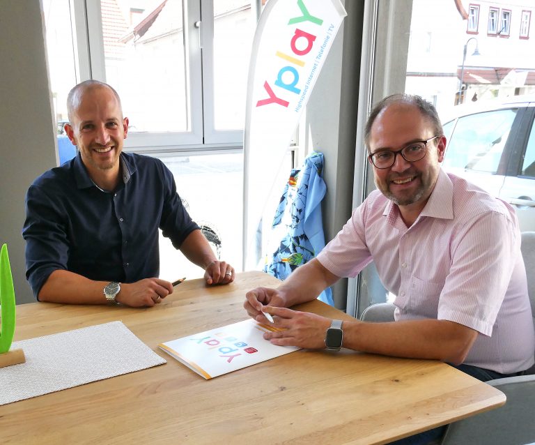 Geschäftsführer Peer Kohlstetter und Bürgermeister Dominik Brasch sitzen am Tisch vor Yplay Fahne und unterzeichnen Absichtserklärung zum Glasfaserausbau in Bad Soden-Salmünster