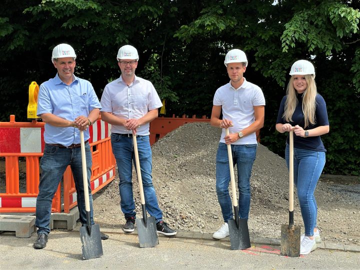 Gruppe von Personen stehen vor Sandhaufen mit Yplay Bauhelmen und Spaten zum Spatentisch für den Glasfaserausbau in Hammersbach