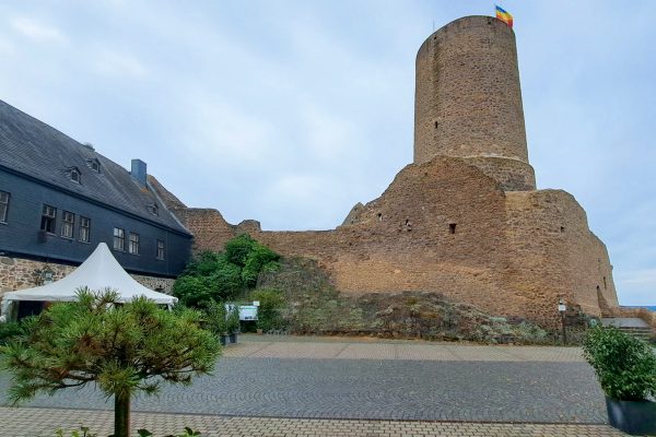 Mittelalterliche Mauerreste und Turm vor gepflastertem Platz mit Kübelpflanzen in Wettenberg